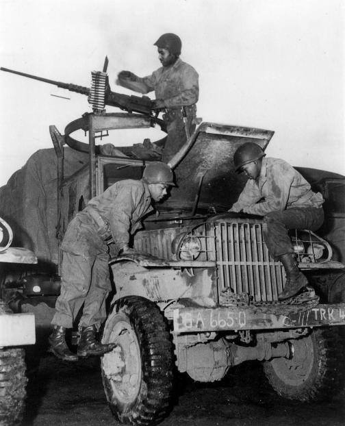 African American members of the World War II Red Ball Express repair a CCKW 2 truck while a crewman at a machine gun keeps watch for aircraf.jpg
